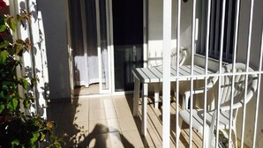 A balcony with a white table and chairs, a sliding glass door, and a view of the street. - Apartment in Kato Paphos (Phafos)