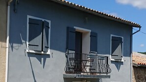 Un bâtiment à deux étages doté d’un balcon, d’une cheminée et d’un jardin où poussent des fleurs roses.