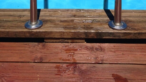 Une terrasse en bois avec des garde-corps métalliques entourant la piscine, offrant une vue sur une piscine à l’eau d’un bleu limpide.