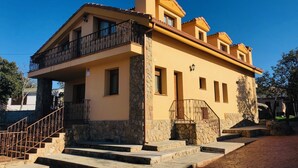 A two-story building with a stone base and yellow walls, featuring a balcony with wrought iron railings and a stone staircase leading to the entrance.