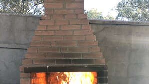 A brick outdoor oven with a fire burning inside, a sink, and a stone wall.