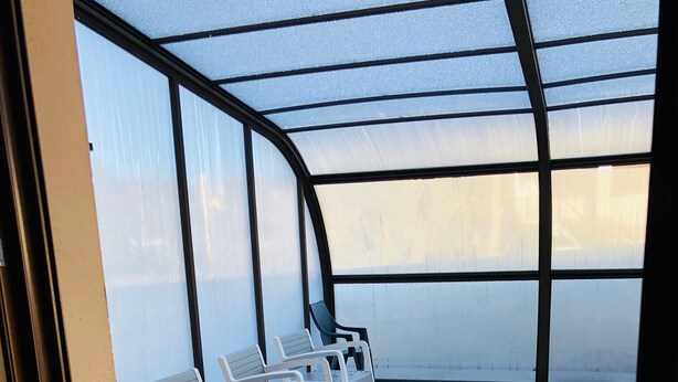 An indoor swimming pool area with a glass ceiling, several white lounge chairs, and a small pool.