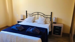 A neatly made bed with a dark blue bedspread and two pillows, a bedside table with a lamp, and a nightstand with a lamp.