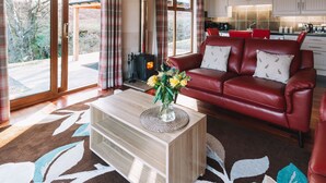 A spacious living room with a red leather sofa, a wooden coffee table with a vase of flowers, and a large window offering a view of the outdoors.