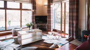 A modern living room with large windows, a flat-screen TV, a fireplace, and a wooden coffee table.