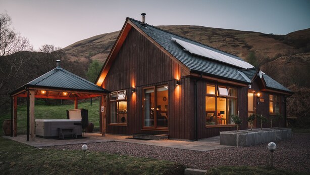 A wooden cabin with a covered patio, large windows, and a metal roof.