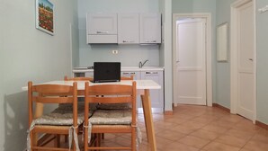 Un coin repas avec une table et des chaises, un ordinateur portable posé sur la table, et une cuisine en arrière-plan.