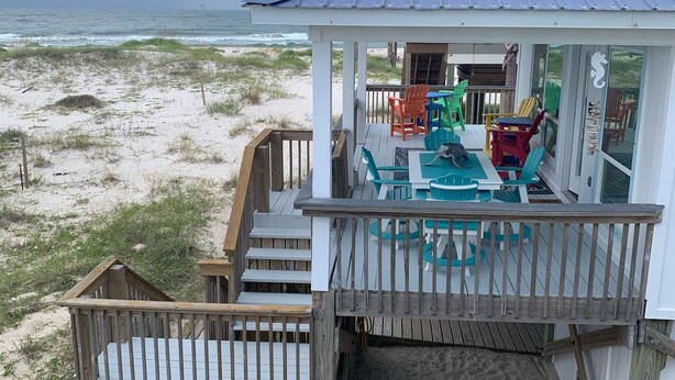 Ein Strandhaus mit Terrasse, Sitzgelegenheiten im Freien und Blick auf den Ozean.