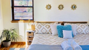 Un dormitorio ordenado con una cama grande, una planta en maceta y una ventana con persianas.