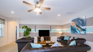 A modern living room with a ceiling fan, leather sofas, a flat-screen TV, and a large abstract painting. - 5Star Resort/Clean and Safe/Mins to Parks/WaterPark/Arcade/Bar/Gym/Golf/AC/WiFi (Davenport)