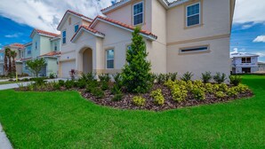 A residential building with a light beige exterior, red-tiled roof, and a well-maintained lawn with various shrubs and a small tree. - 5Star Resort/Clean and Safe/Mins to Parks/WaterPark/Arcade/Bar/Gym/Golf/AC/WiFi (Davenport)