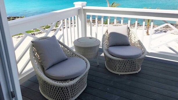 A deck with wicker chairs and a small round table, overlooking a beach with clear blue water. - New Oceanfront Home with Dock, Kayaks, Private Pool (Governors Harbour)