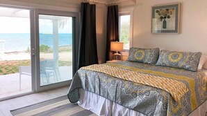 A bedroom with a large bed, a sliding glass door to a balcony, and a framed artwork on the wall. - New Oceanfront Home with Dock, Kayaks, Private Pool (Governors Harbour)