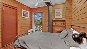 A wooden room with a bed, a radiator, a shelf with baskets, and a door. - 41 Carlo Circle - Rainbow Beach. Huge Beach House With Room for Everyone! (Rainbow Beach)