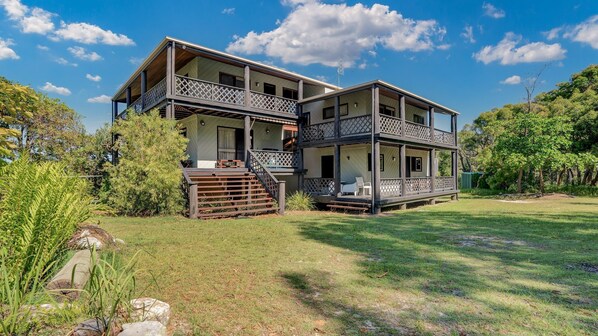 A two-story house with a covered porch and a small deck, surrounded by a grassy yard and trees. - 41 Carlo Circle - Rainbow Beach. Huge Beach House With Room for Everyone! (Rainbow Beach)