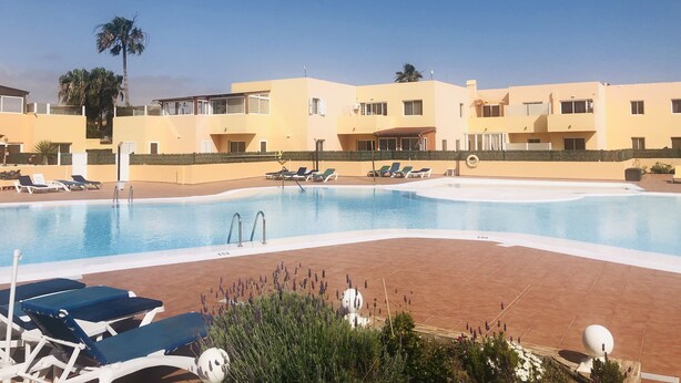 Une piscine avec des chaises longues et un bâtiment doté de nombreux balcons.