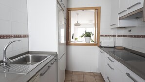 Een compacte keuken met een roestvrijstalen spoelbak, witte kastjes, een raam met uitzicht en een broodrooster op het aanrecht.