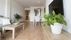 Een moderne woonkamer met een bank, een salontafel, een plant in pot, een televisie en een bureau met stoel.