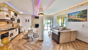A modern living room with a sofa, dining table, and kitchen area with a stove and cabinets. - 3 bedroom amazing home in Grab (Grab)