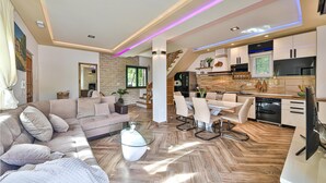 A modern living room with a sofa, a glass coffee table, and a dining area with a table and chairs. - 3 bedroom amazing home in Grab (Grab)