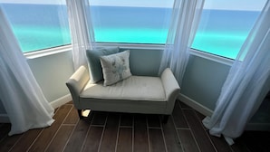 Un balcon doté d’un espace salon avec des coussins, offrant une vue sur l’océan et agrémenté de rideaux légers.