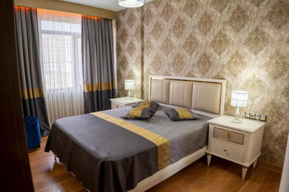 A neatly arranged bedroom with a large bed, two bedside tables, and a window with curtains.