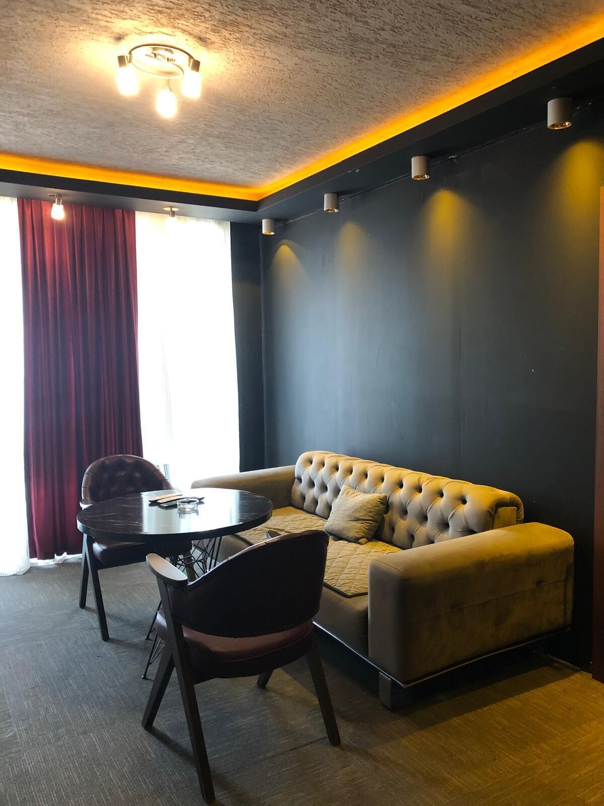 A modern room with a dark wall, a tufted sofa, a round table, and two chairs.