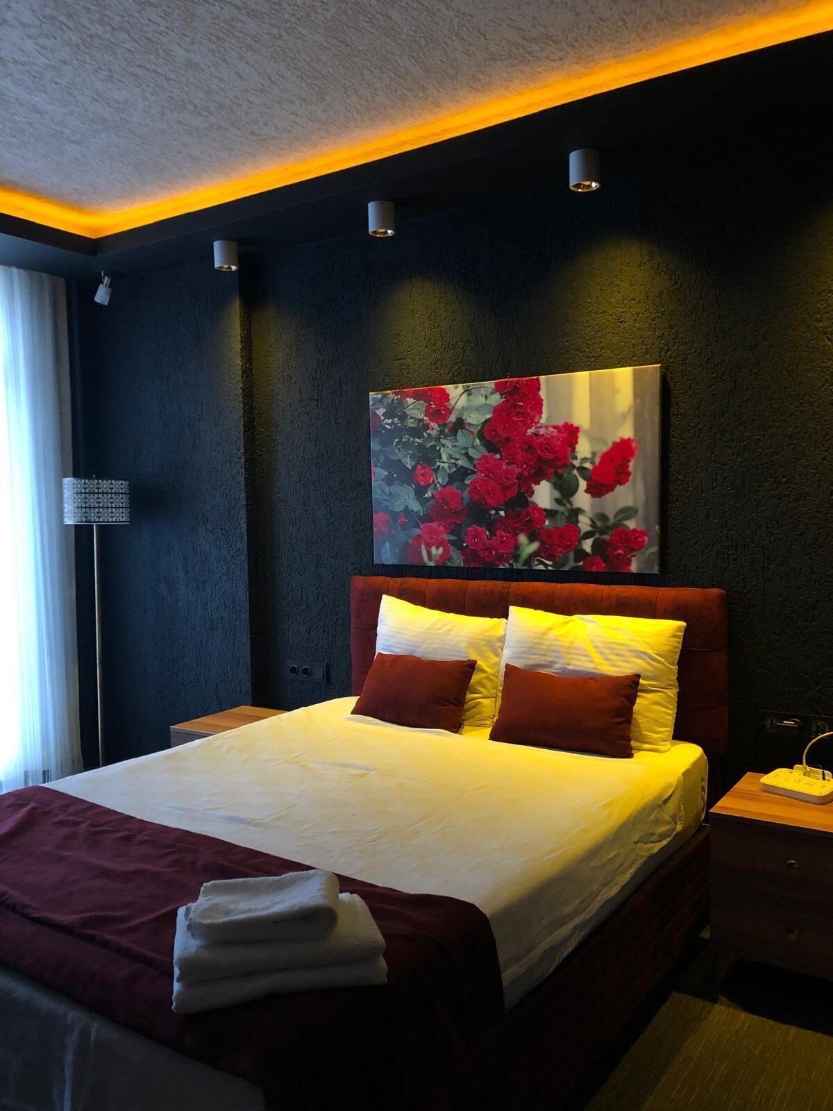 Ein modernes Hotelzimmer mit einem großen Bett, einem Gemälde von roten Blumen an der Wand und einem Nachttisch mit einer Lampe.
