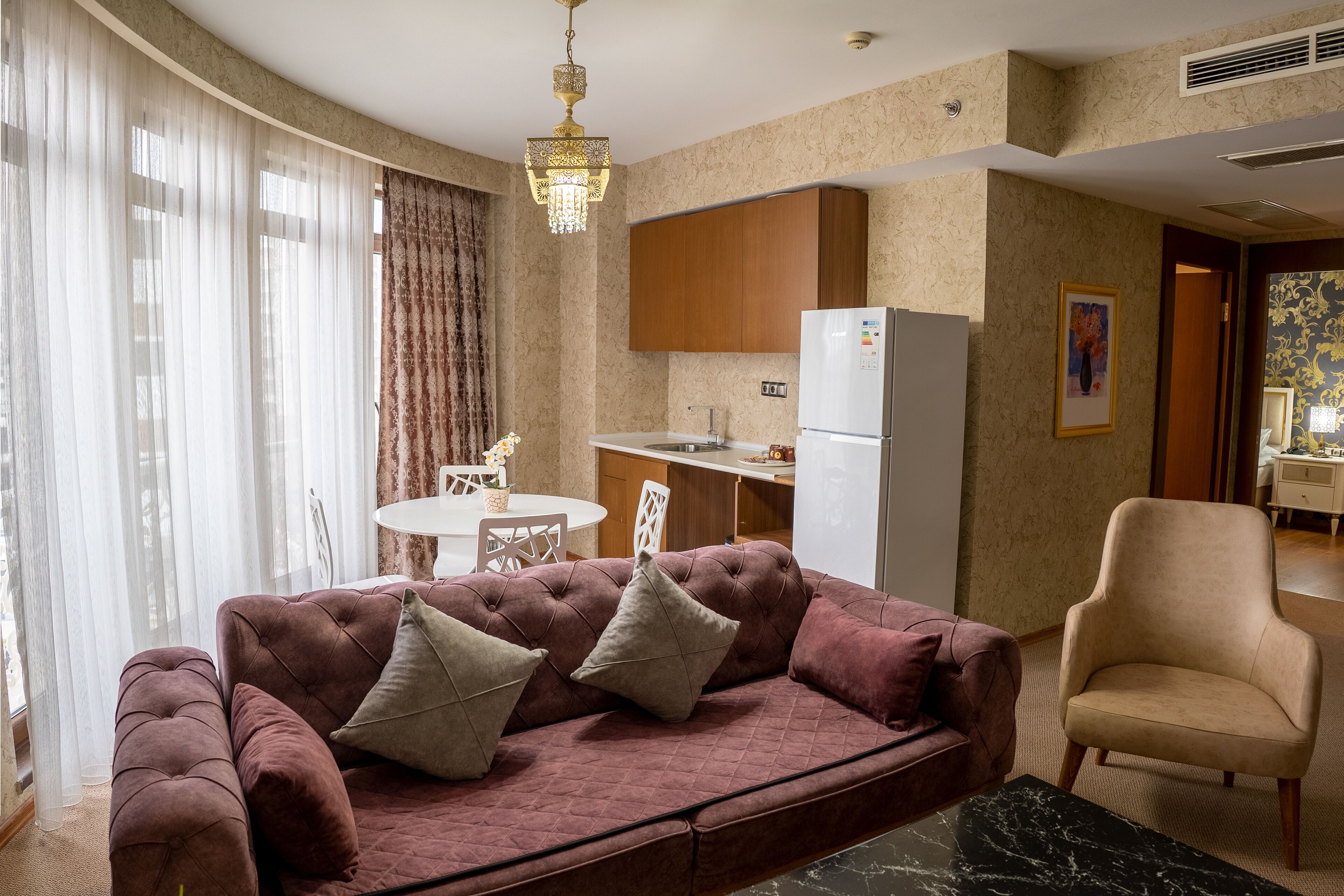 Una sala de estar con un sofá rojo, un sillón beige y una zona de comedor con una mesa y sillas blancas.
