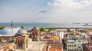 Un paisaje urbano costero con edificios históricos, una cúpula destacada y vistas al mar.