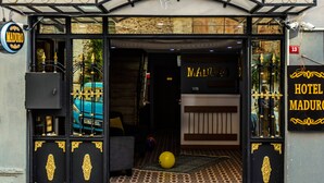 Fachada de hotel en negro y dorado, con puerta de vidrio y un pequeño felpudo verde en la entrada.