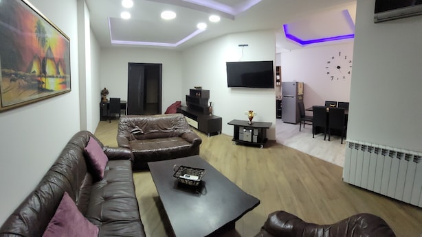 Een woonkamer met een bruine leren bank, een donkere salontafel en een flatscreen televisie aan de wand.