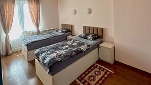 Een moderne slaapkamer met twee bedden, een houten vloer, een kamerkleed met patroon, en een raam met gordijnen.