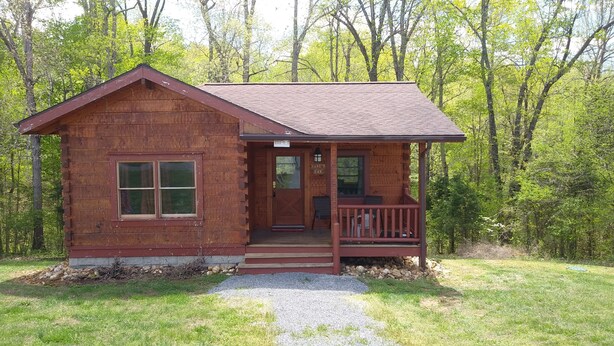 A small wooden cabin with a porch, surrounded by trees. - Bleidt's Buck Cabin (Cadiz)