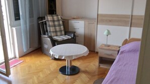 A bedroom with a bed, a chair, a desk, a table, and a wardrobe.