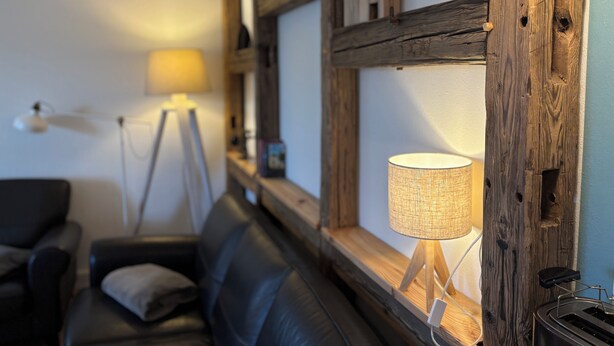 A cozy living room with a black leather sofa, a standing floor lamp, and a table lamp. - Vacation apartment Zur alten Schäferei with sauna in the historic four-sided courtyard (Zeulenroda-Triebes)