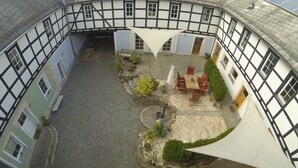 A courtyard with cobblestone flooring, a seating area with a table and chairs, and a white canopy. - Vacation apartment Zur alten Schäferei with sauna in the historic four-sided courtyard (Zeulenroda-Triebes)