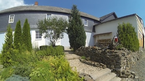 A house with a stone wall and a garden with various plants and a tree. - Vacation apartment Zur alten Schäferei with sauna in the historic four-sided courtyard (Zeulenroda-Triebes)