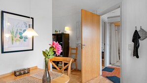 Une pièce avec une table à manger en bois, un vase rempli de fleurs, un tableau encadré accroché au mur, une porte en bois donnant sur une autre pièce, et un manteau suspendu au mur.
