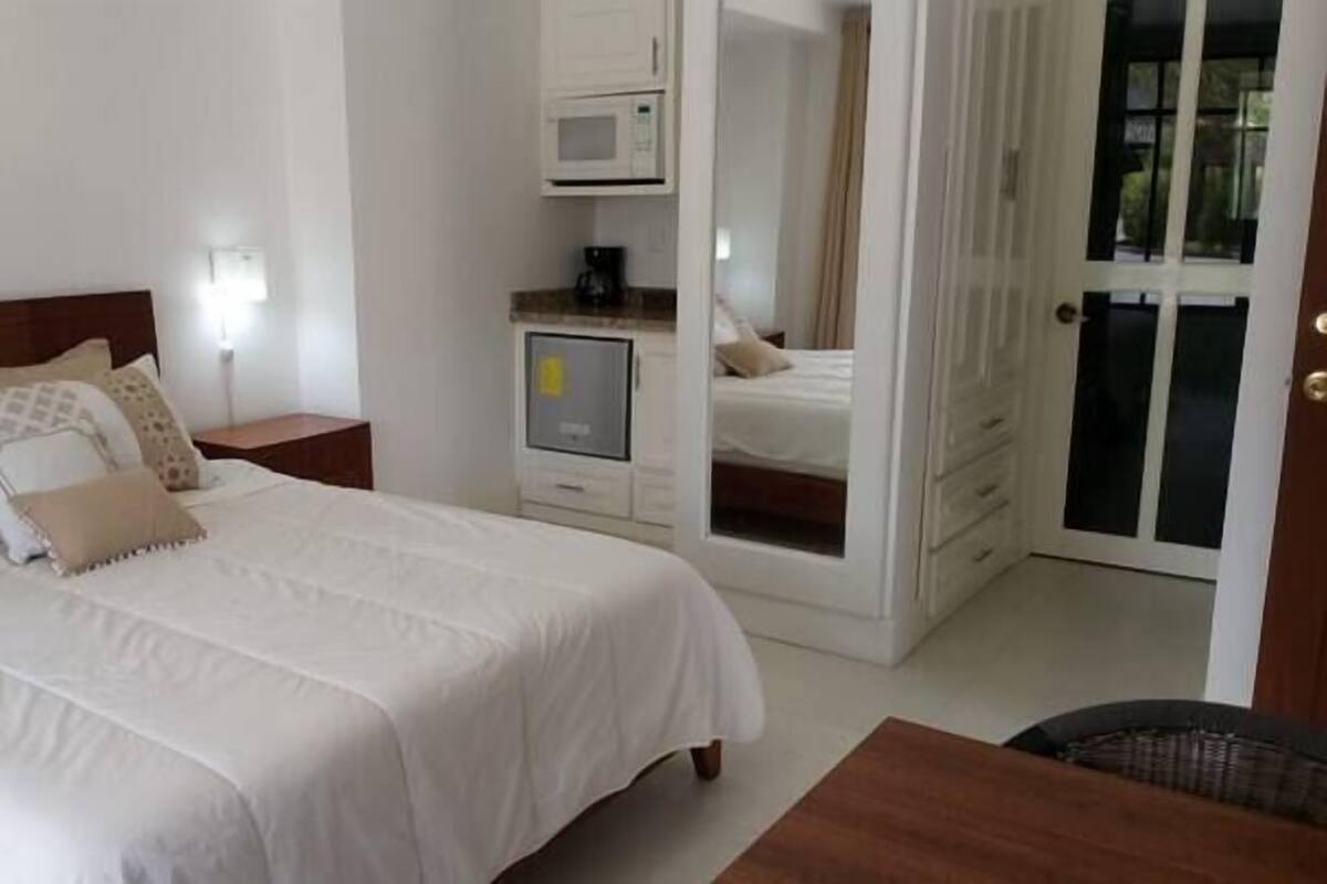 Un dormitorio con cama, mesitas de noche, armario, microondas y vistas a través de una puerta.