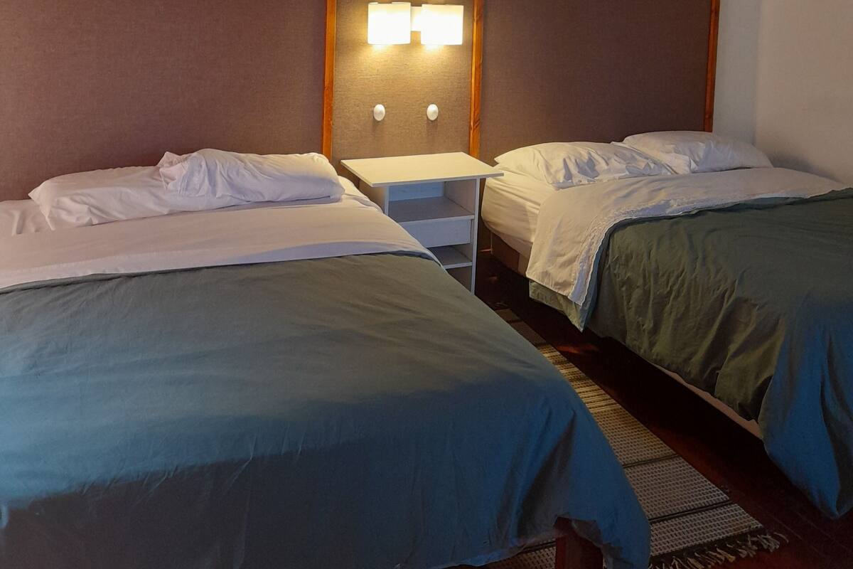Una habitación de hotel con dos camas, un cabecero de madera y una mesita de noche con lámpara.