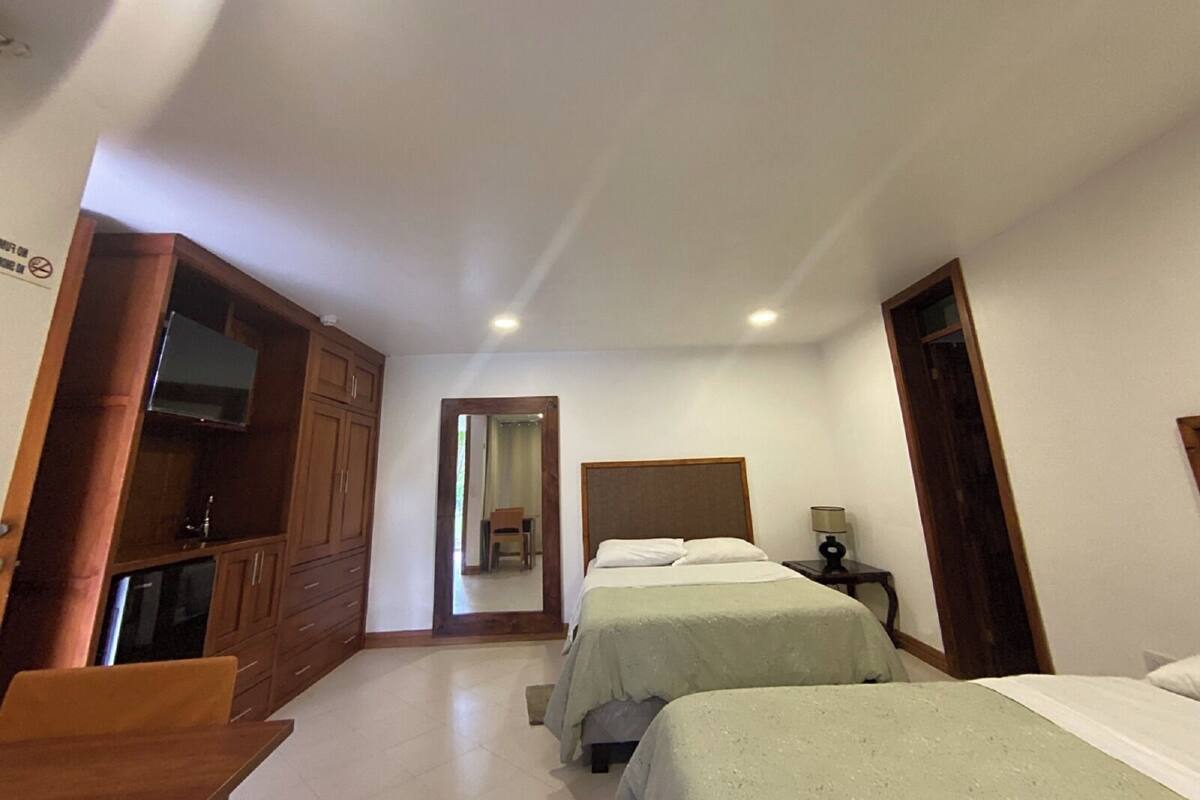 Una habitación de hotel con dos camas, un armario de madera, un televisor y un espejo.