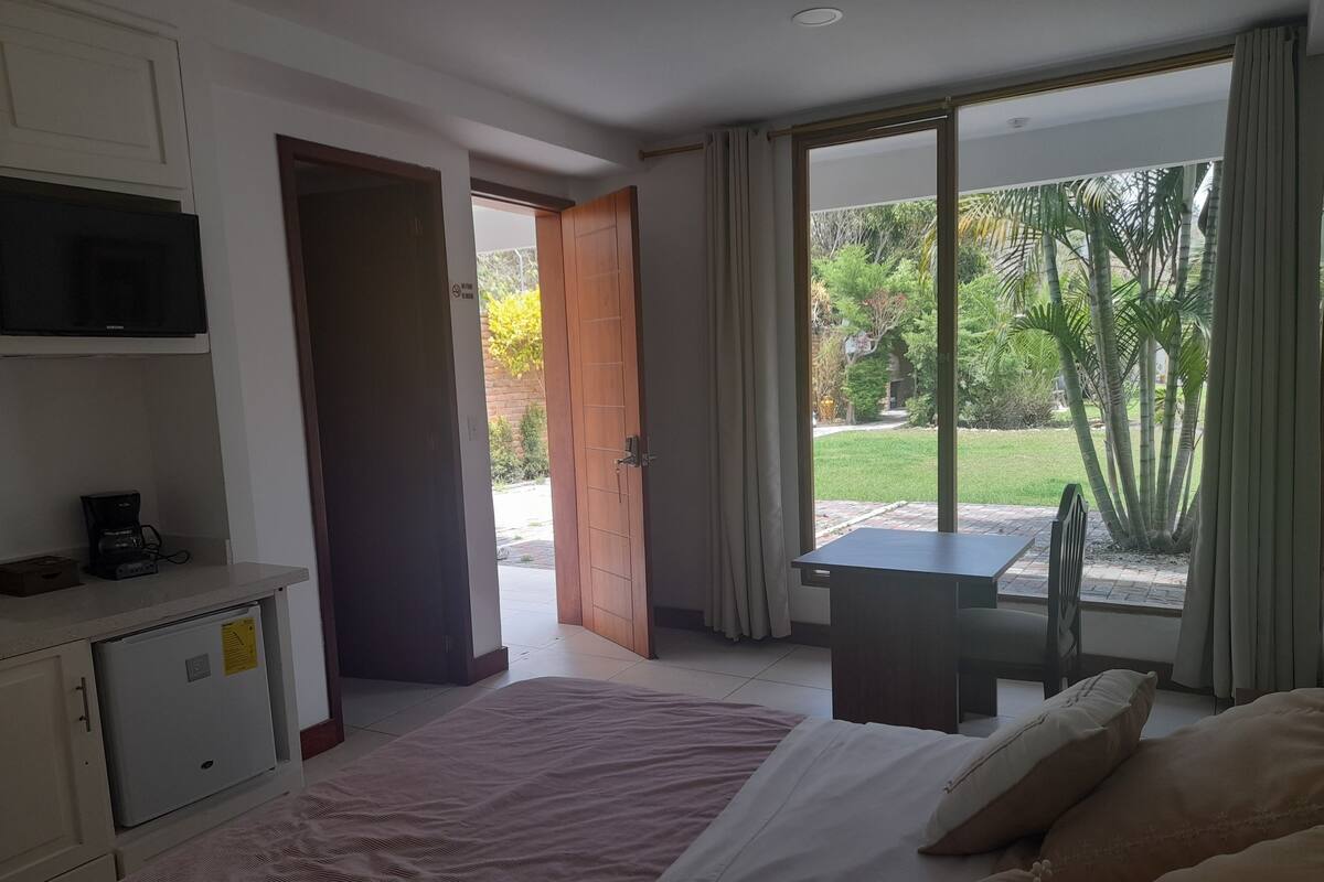 Una habitación de hotel con una cama, un escritorio, un televisor y vista al jardín.