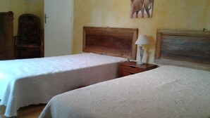 A room with two beds, wooden headboards, a nightstand with a lamp, a chair, and a painting on the wall.