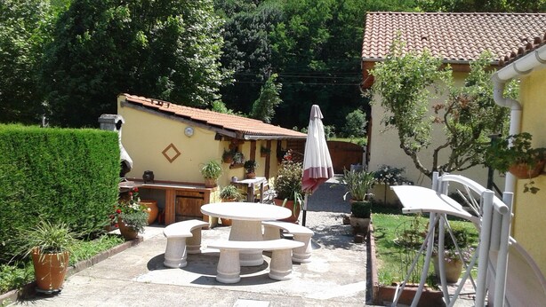 A patio with a round table and chairs, surrounded by potted plants and a small outdoor kitchen area.