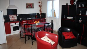 A compact kitchen with a dining area, a red chair, and a black sofa with a red cushion.
