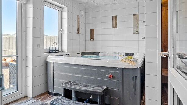 A modern bathroom with a large bathtub, a window, and a wooden door. - Cozy home in Thyborøn with sauna (Thyborøn)