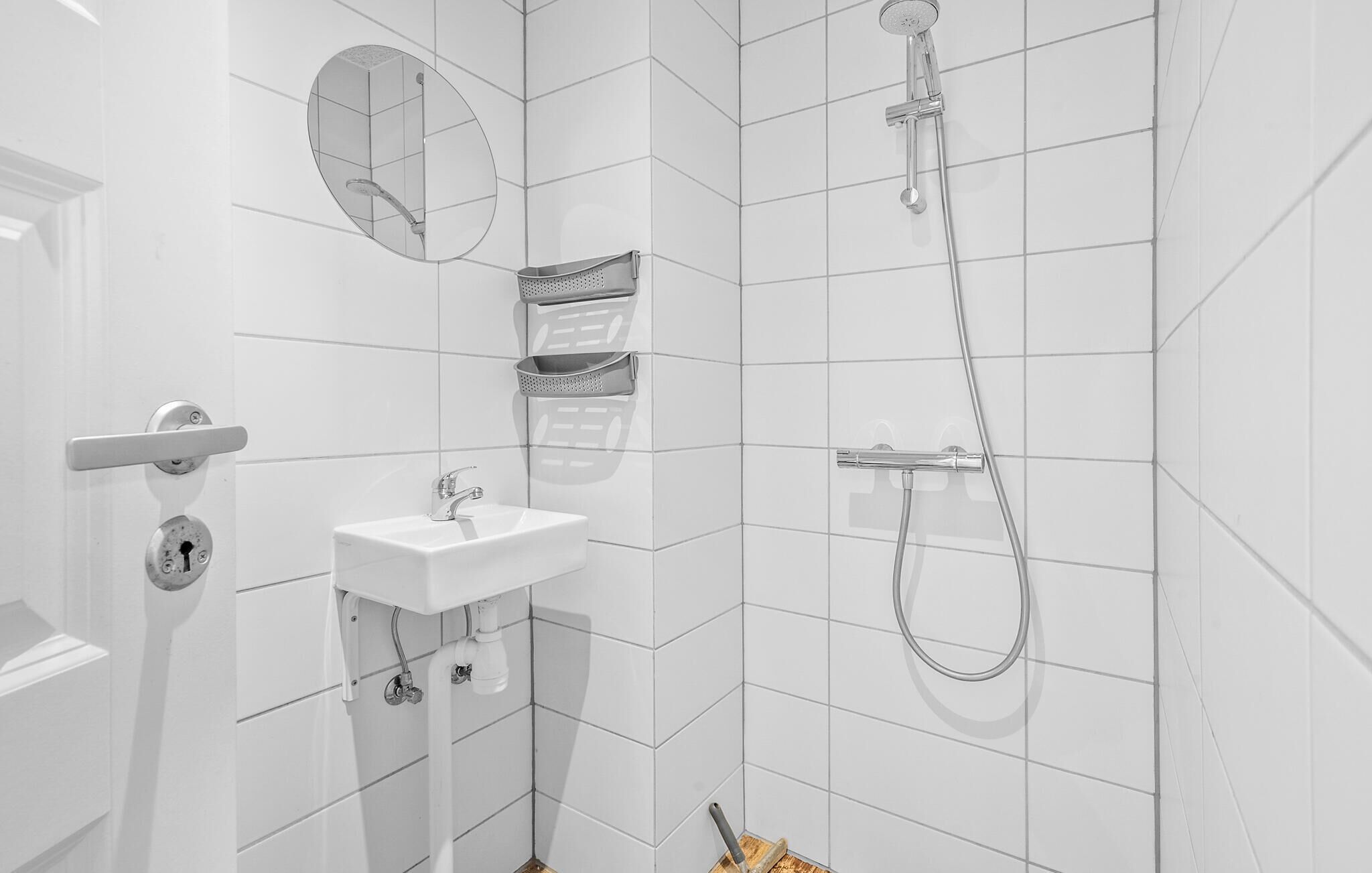 Casa de banho com azulejos brancos, uma pia, espelho e chuveiro.