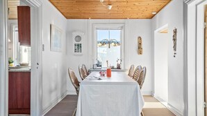 A dining area with a long table, wicker chairs, a white tablecloth, and a window with a view. - Cozy home in Thyborøn with sauna (Thyborøn)