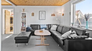 A modern living room with a sectional sofa, a round coffee table, and a bookshelf. - Cozy home in Thyborøn with sauna (Thyborøn)